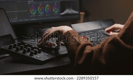 Female editor works in studio, uses digital color grading control panel. Colorist makes video color correction on computer. Program interface with RGB graphics, color wheels and levels on PC monitor.