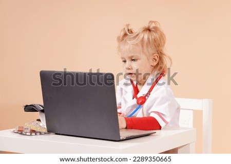 A child as a doctor with a toy stethoscope takes notes in a laptop and keeps a patient's medical history.