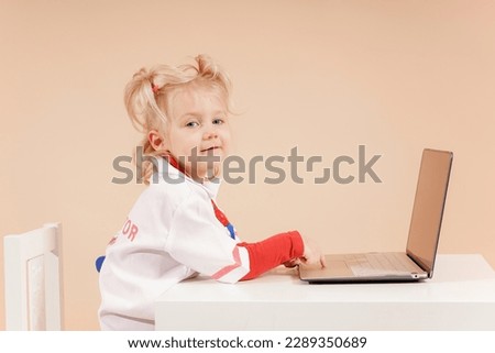 A little girl doctor sits at a laptop as a doctor and takes patients making notes in a laptop.