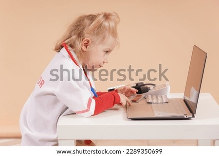 A child as a doctor with a toy stethoscope takes notes in a laptop and keeps a patient's medical history.