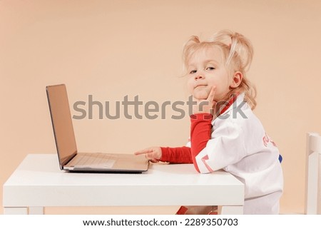 Little girl doctor sits at a laptop as a doctor and looks into the camera.