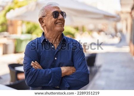 Senior grey-haired man smiling confident standing with arms crossed gesture at street