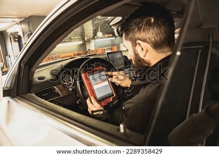 A mechanic's hands use a diagnostic tool to troubleshoot a modern car's computer system in a garage. Royalty-Free Stock Photo #2289358429