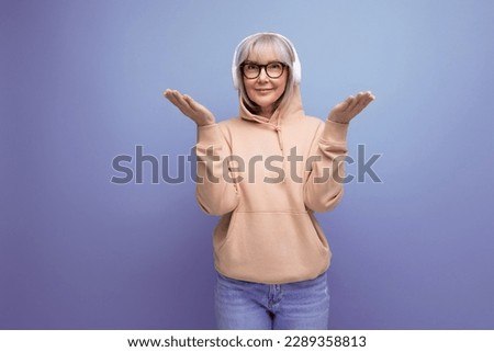 stylish grandmother with gray hair masters technique and listens to music in headphones on a studio background with copy space
