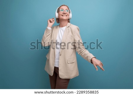 close-up portrait of a 50s middle-aged business woman in a jacket listening to music with headphones on a studio background with copy space