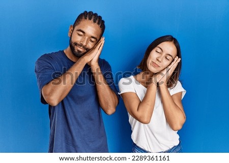 Young hispanic couple standing together sleeping tired dreaming and posing with hands together while smiling with closed eyes. 