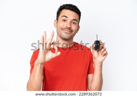 Young handsome man holding car keys over isolated white background showing ok sign with fingers