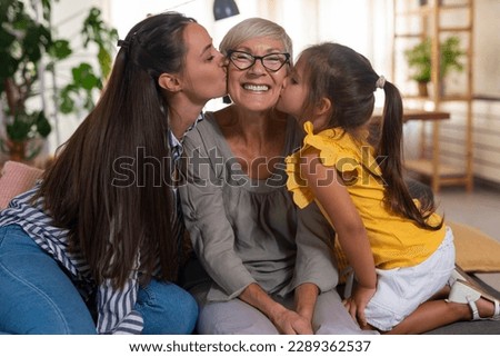 Three generations of women. Beautiful woman and little girl are kissing their granny while sitting on couch at home