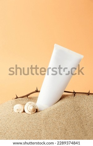 Tube with cream, shells and branches on sand against orange background. Cosmetic product