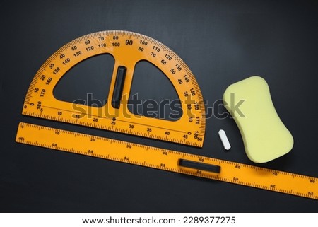 Ruler, protractor, chalk and sponge on black table, flat lay