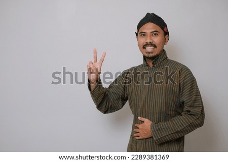 Asian man wearing javanese costume and give V finger sign at special blank background