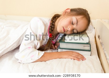 Conceptual portrait of little girl using pile of books instead of pillow