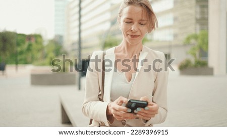 Businesswoman with blond hair sitting on a bench typing on cellphone on cellphone