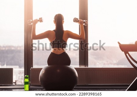 Young woman at sunrise at home doing workout with dumbbells. View from the back. Healthy sport lifestyle concept.