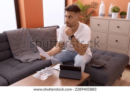 Young hispanic man reading document accounting at home