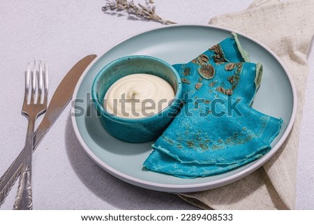 Thin blue pancakes with creamy sauce. Healthy vegan non lactose and gluten free food, breakfast concept. Trendy hard light, dark shadow, light stone concrete background, close up