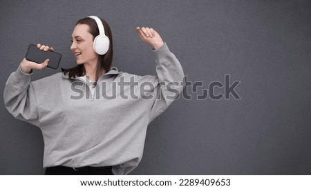 A young teenager girl listens to music with headphones, dressed in a black jacket and jeans, dances to the music and sings songs loudly
