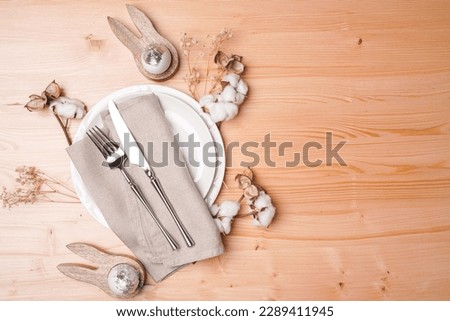 A top view on a Empty white ceramic plate, silver cutlery on linen napkin, cotton flower decoration on a wooden background, copy space, top view