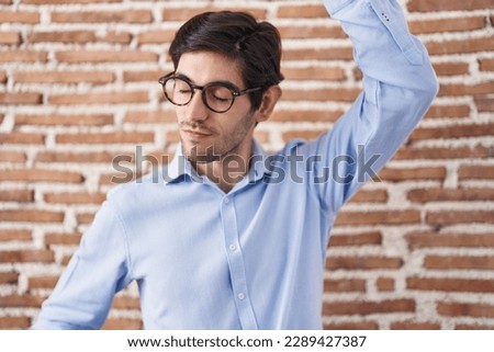 Young hispanic man standing over brick wall background dancing happy and cheerful, smiling moving casual and confident listening to music 