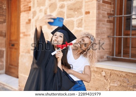 Two women mother and graduated daughter make selfie by smartphone at campus university