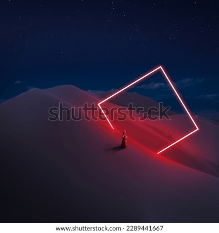 Modern futuristic neon abstract background. Large square rectangle glowing red object in the center of sand dune and lonely Indian woman silhouette in traditional dress in the desert.  Royalty-Free Stock Photo #2289441667