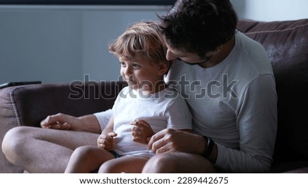 Playful dad and son relationship. Child seated on father lap on couch at home. Authentic real life fatherhood lifestyle Royalty-Free Stock Photo #2289442675