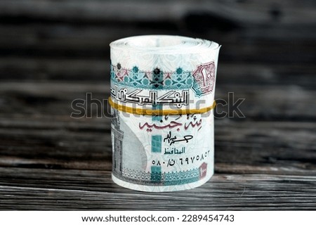 100 EGP LE one hundred Egyptian pounds cash money bills rolled up with rubber band, Egypt money roll pounds  features Sultan Hassan mosque and the Sphinx of Giza isolated on wooden background Royalty-Free Stock Photo #2289454743