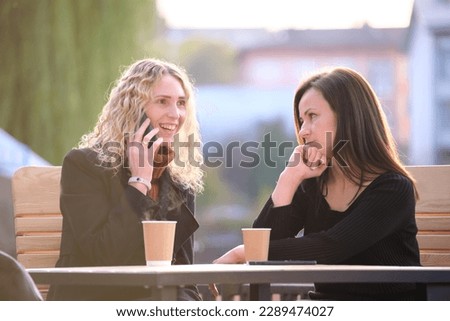 Unhappy young woman waiting angrily while her friend is talking happily on sellphone with someone else and ignoring her. Friendship problems concept Royalty-Free Stock Photo #2289474027