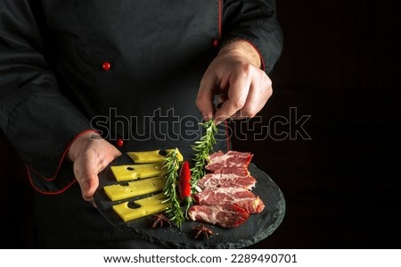 Professional chef puts rosemary on a plate with sliced ham and cheese. The concept of serving dishes to order by a waiter with a place for advertising on a black background