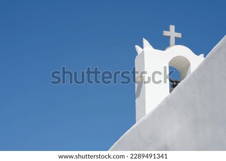 A cross on the top of an orthodox whitewashed church in Ios Greece and a blue sky in the background in Ios Greece