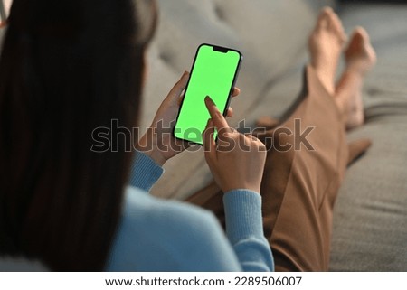 Young woman home use green screen mockup Smartphone, her sitting on sofa in living room
