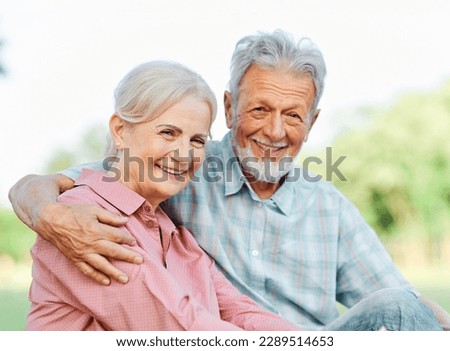 Happy active senior couple having fun talking and hugging sitting on a bench in park outdoors