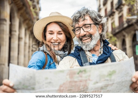 Married couple of tourists sightseeing city street with map - Happy husband and wife enjoying summer vacation together - Touristic life style concept with aged woman and man traveling European city Royalty-Free Stock Photo #2289527517