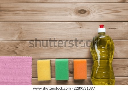 Dishwashing set. Copy space. Top view. Kitchen cleaning sponges, detergent liquid, microfiber cloth on wooden table background with place for text. Routine everyday housework.