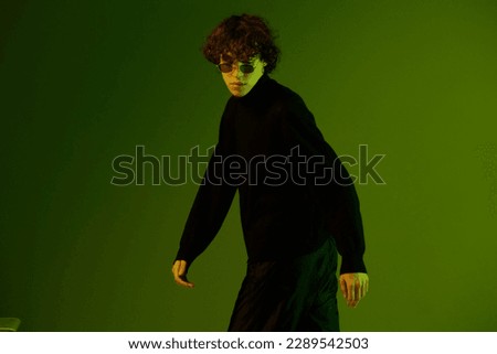 Man dancer in glasses fashion and style smile model poses dance, hipster party teen lifestyle, portrait green background mixed neon light, copy space
