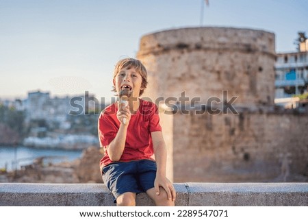 Boy tourist eating turkish ice cream on background of Hidirlik Tower in Antalya against the backdrop of the Mediterranean bay of the ancient Kaleici district, Turkey. Turkiye