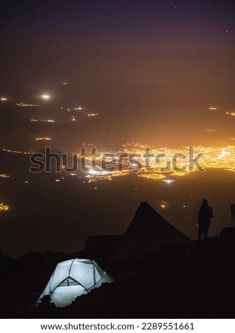 The city of Dogubayazit glows at night from the slope of Mount Ararat, a tent in the foreground