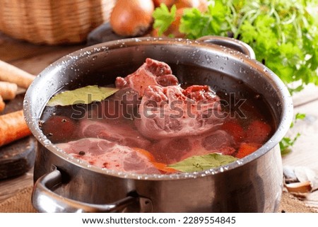 Raw veal beef Oxtail Meat with carrots, onions and spices in a saucepan on the wooden table. Bone Broth Bouillon preparation