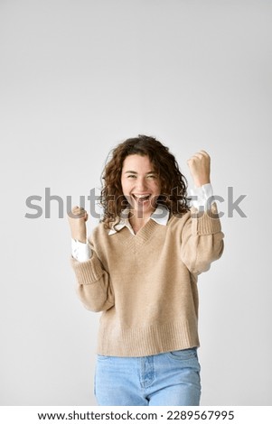Young happy lucky funny woman student feeling amazed and excited winner raising fists in yes gesture celebrating professional win achievement, rejoicing success standing at white background. Royalty-Free Stock Photo #2289567995