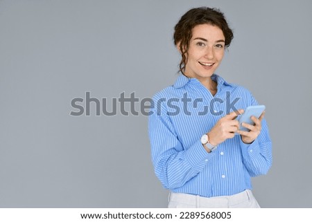 Young business woman professional manager worker holding mobile phone standing isolated at gray wall using cell phone for work, checking apps on cellphone, typing on smartphone tech device.