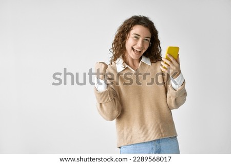 Young happy excited pretty woman student feeling winner holding cellphone using mobile phone winning game app prize, receiving great job offer celebrating standing isolated at white background.