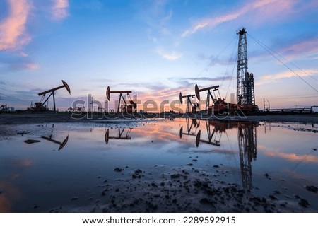Oil field site, in the evening, oil pumps are running, The oil pump and the beautiful sunset reflected in the water, the silhouette of the beam pumping unit in the evening.