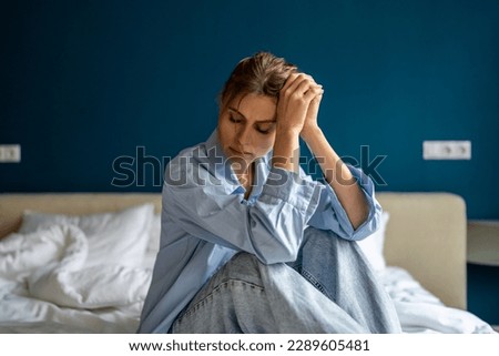 Young unhappy woman sitting on bed at home, waking up depressed, suffering from depression, feeling sad and miserable. Female suffering from post-traumatic stress disorder. Women and mental health Royalty-Free Stock Photo #2289605481