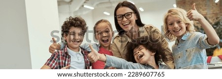 We are the best. Happy school team of four cute little pupils and their friendly female teacher posing together, standing in the classroom Royalty-Free Stock Photo #2289607765