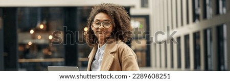Happy african business woman working laptop while sitting outside on background of office building Royalty-Free Stock Photo #2289608251