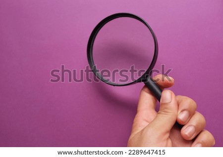 man hand holding a black frame a magnifying glass on Rectangle shape colored paper white and purple background