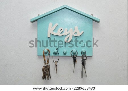 a key ring in the shape of a blue house with the words Keys taped to a white wall