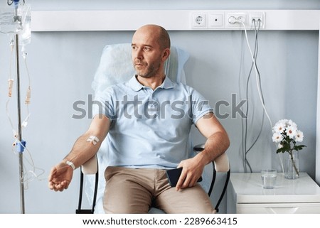 Portrait of adult man sitting in comfortable chair with IV drip during treatment session in clinic Royalty-Free Stock Photo #2289663415