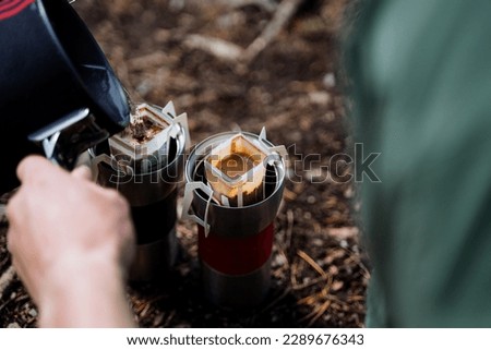 A tourist on a hike brews coffee, a morning ritual to drink a hot drink, camping in nature in the forest, filtering a coffee drink package. High quality photo