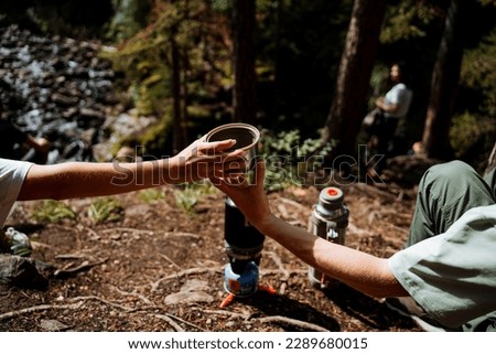 Pass a mug of tea to a friend, hands hold a glass of tea, a person passes a glass of drink to another, breakfast in nature, camping in the forest, camping on a hike, a halt. High quality photo